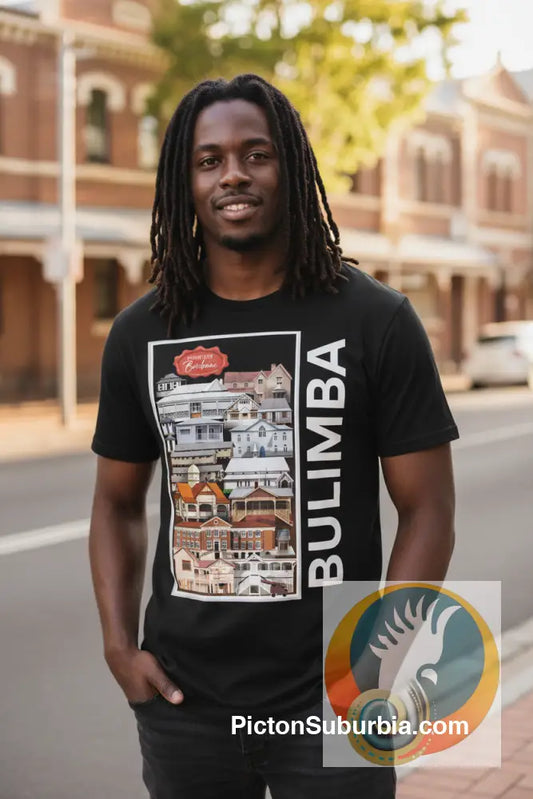A black short-sleeve t-shirt with a graphic print on the front. The graphic features a vertical split design: the left side shows a collage of colorful houses, and the right side has the word 'BULIMBA' printed vertically in white on a black background.